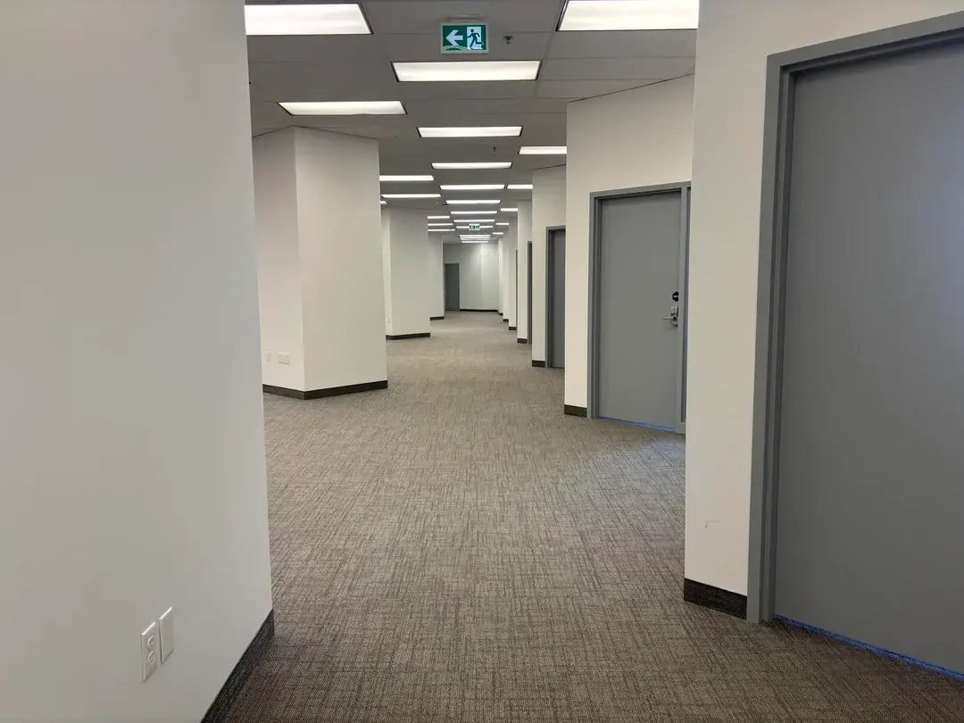 A long hallway with white walls and a blue exit sign.